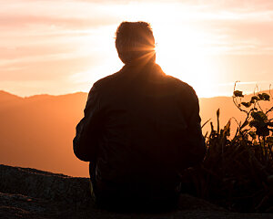 man sitting on hill at sunset