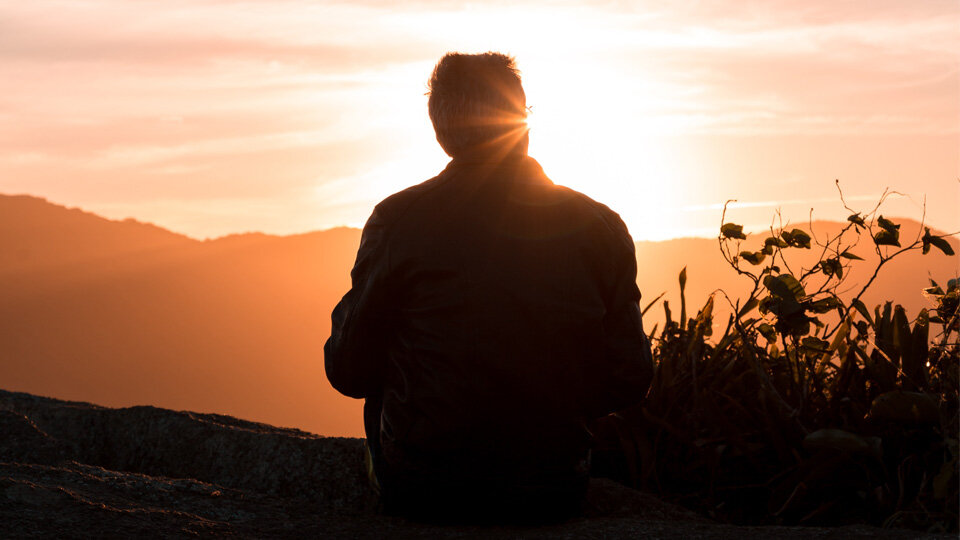 man sitting on hill at sunset