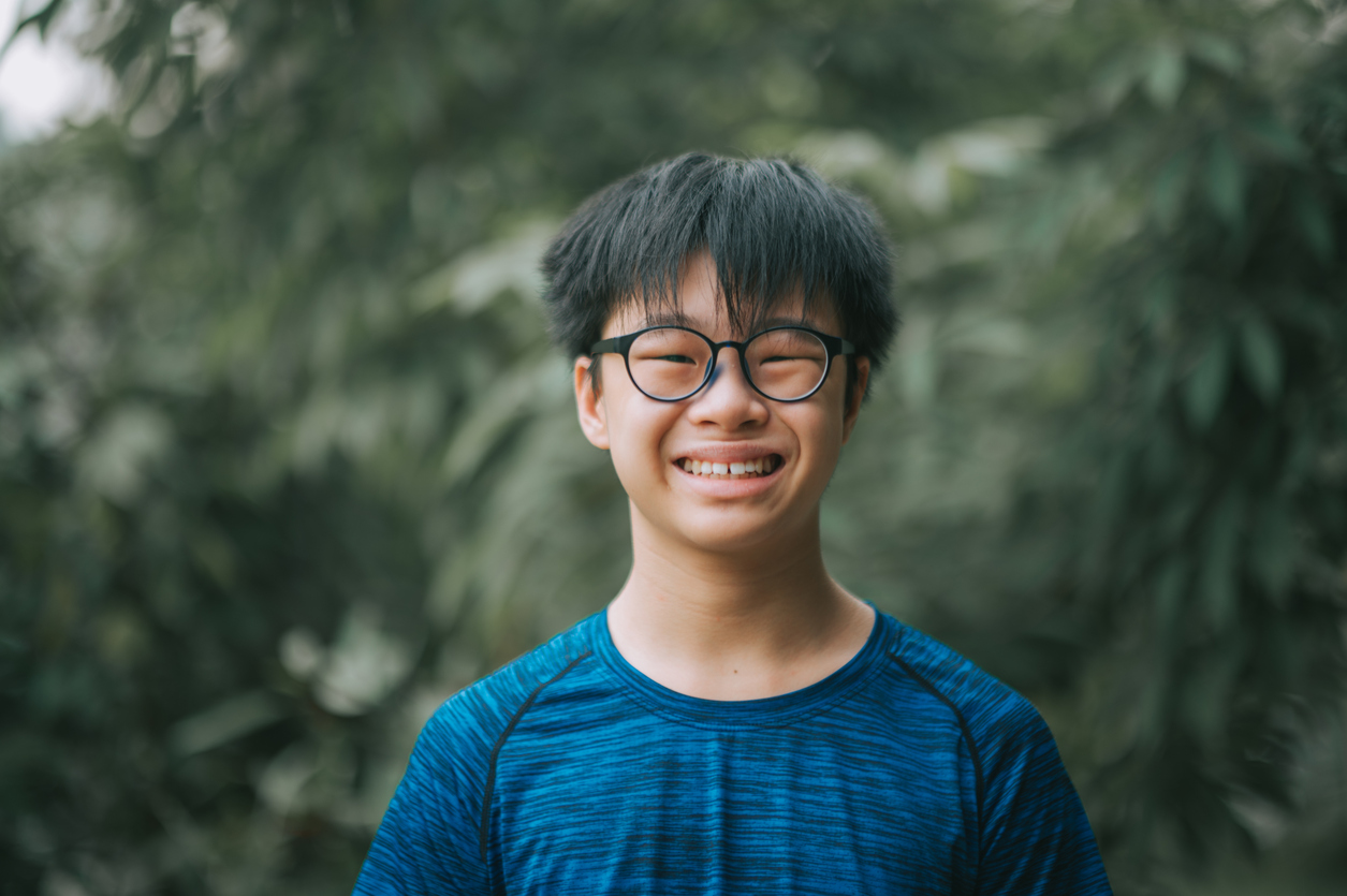 asian chinese teenage boy with eyeglasses looking at camera smiling at backyard of house outdoor