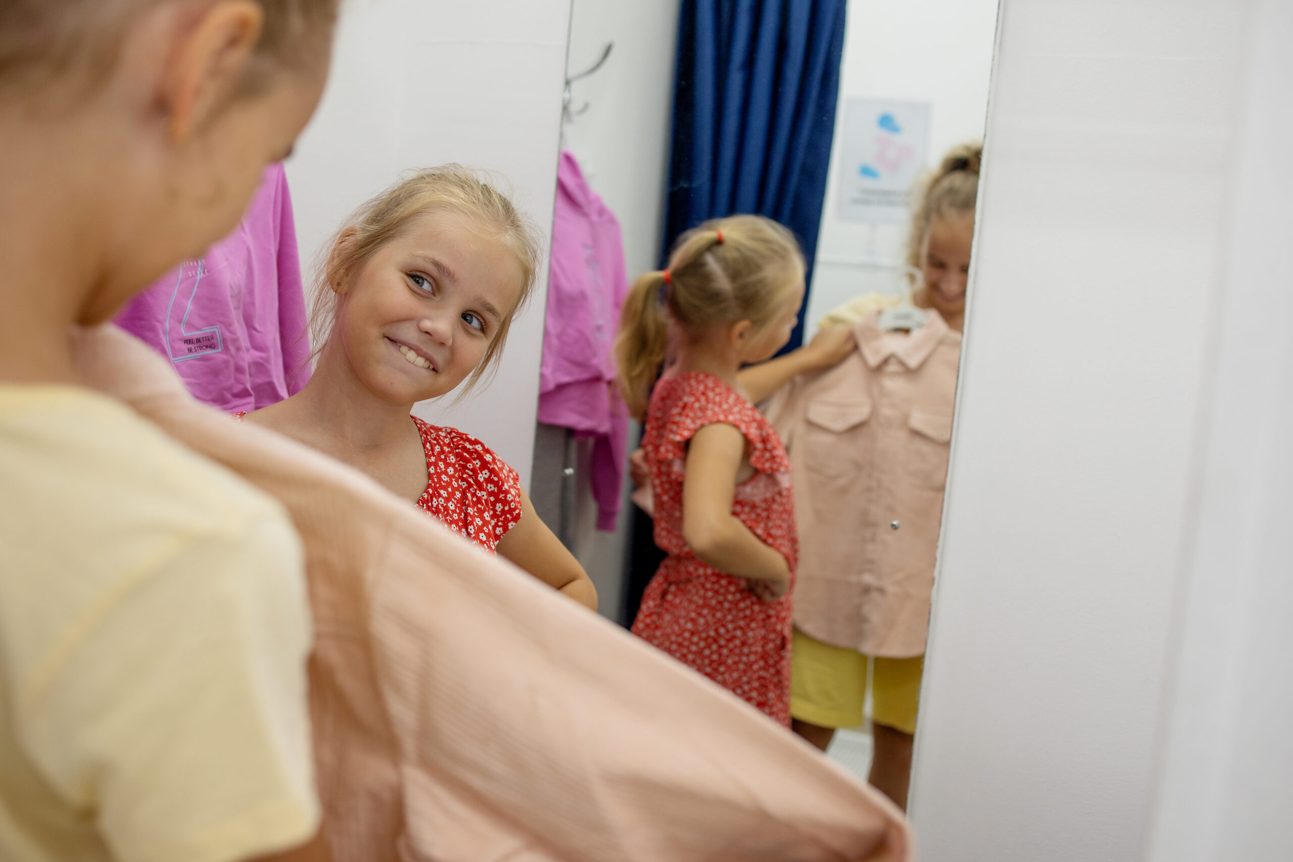 Two cute sister girls are choosing new things in a clothing store. They look at their reflection in the mirror and make a choice. Fun shopping with children