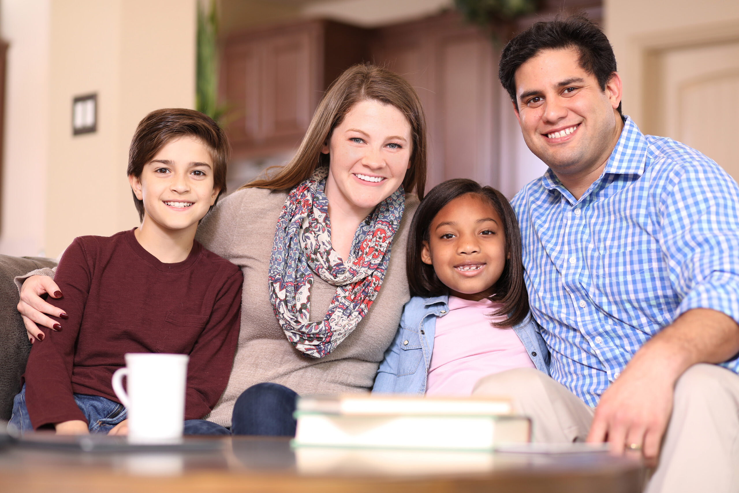 Multi-ethnic family members at home sharing a hug.  Mixed race young couple with adopted or foster care children pose for camera.