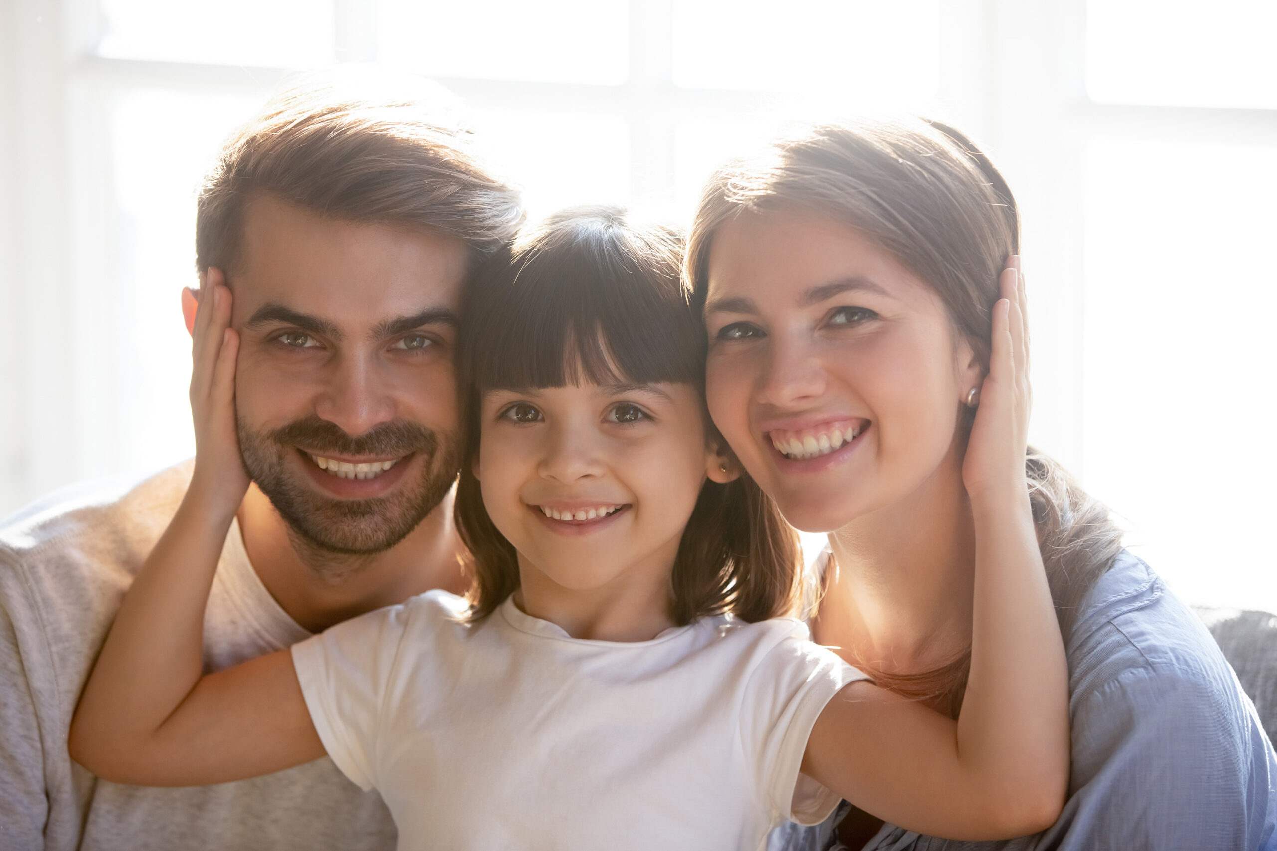 Head shot portrait happy family with little adorable preschool daughter sitting on couch at home posing looking at camera. New parents for adopted child, warm relations, support care wellbeing concept
