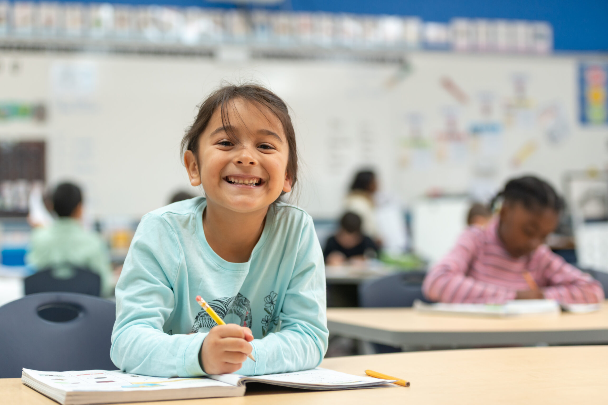 A cute little girl of african descent works hard on her in class assignment. She is working in her math workbook.