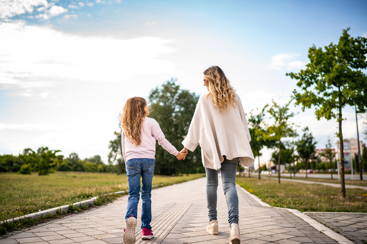 Girl holds her mother's hand and they walk on a sunny day