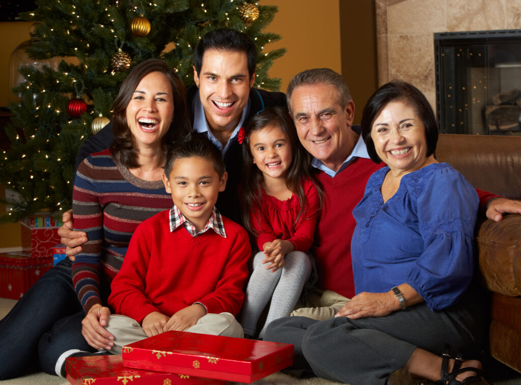 Multi Generation Family In Front Of Christmas Tree Smiling To Camera