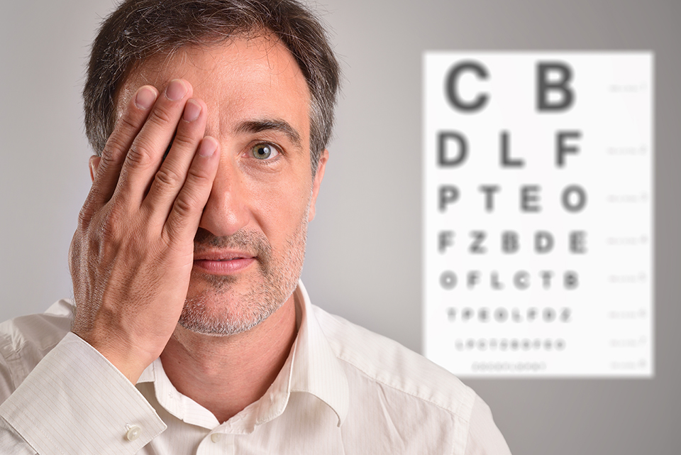 Middle-aged man covering an eye for optical revision with letter chart in the background. Horizontal composition