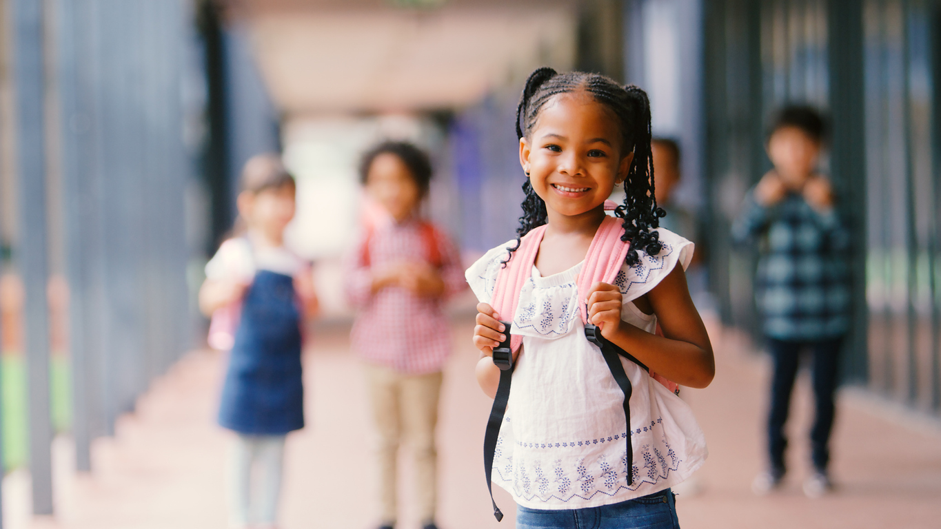 Portrait Of Smiling Female Elementary School Pupil Outdoors With Backpack At School