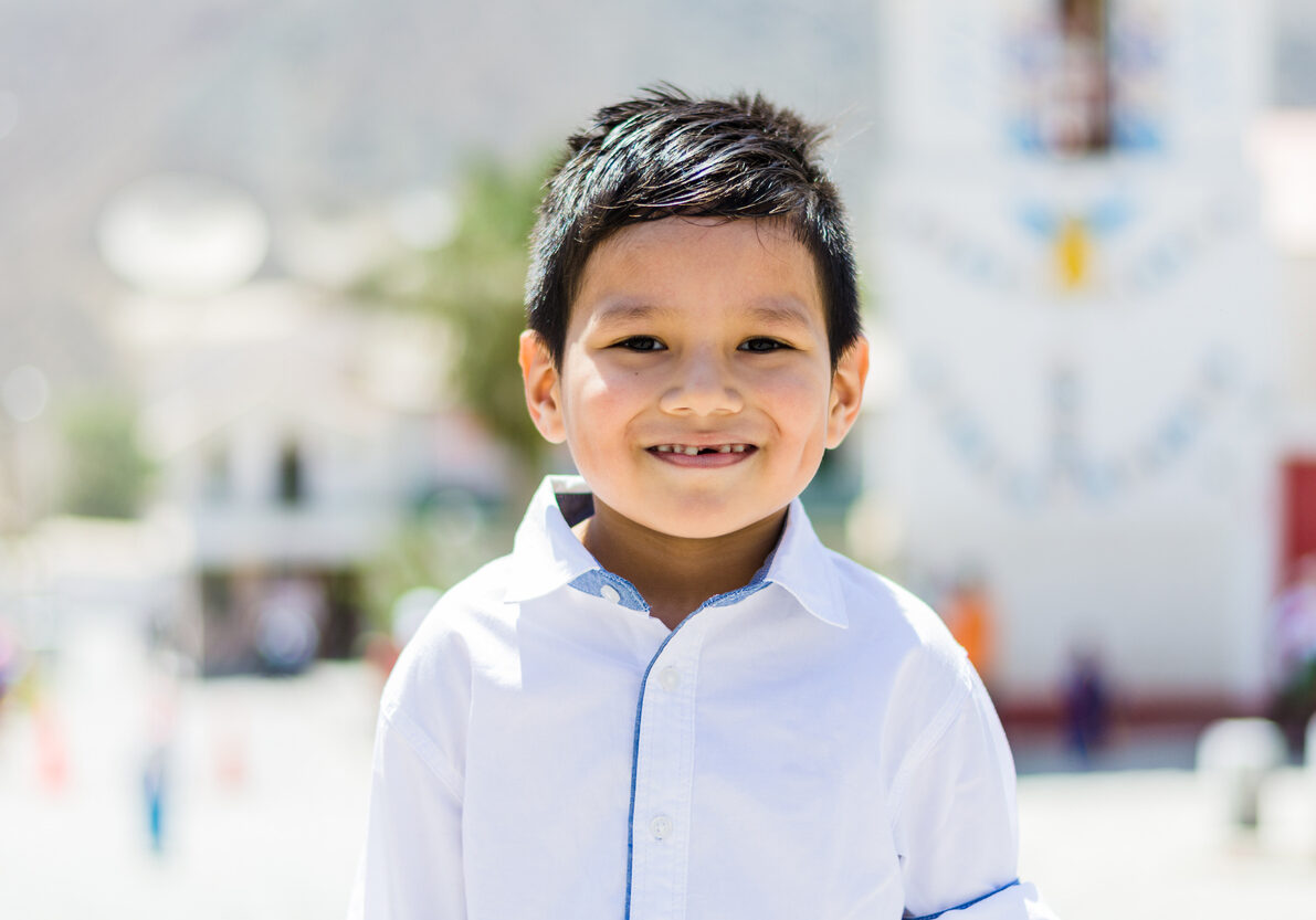 Boy in white shirt outdoors smiling without teeth
