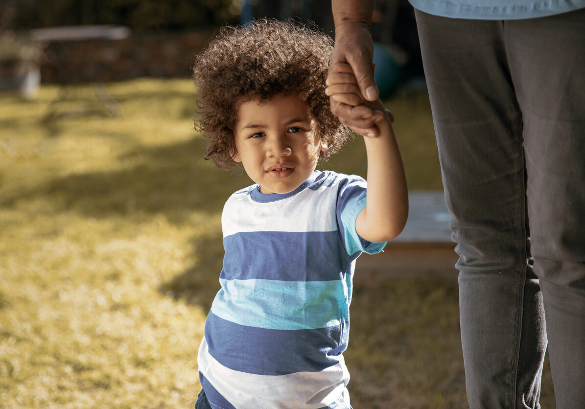 A tender close-up showing a young boy gently holding his grandmother’s hand as they stand together in the garden. A simple and touching moment of love, trust, and connection between generations.
